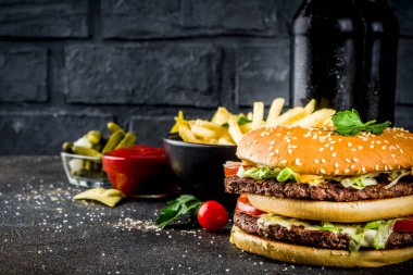 Çeşitli parti gıda, hamburger, patates kızartması, patates cipsi, salatalık turşusu, soğan, domates ve soğuk bira şişeleri, paslı siyah beton arka plan kopya alanı