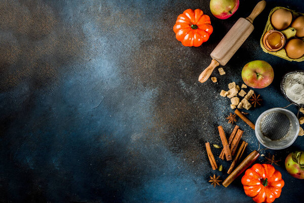 Sweet autumn baking cooking background with flour, rolling pin, decorative pumpkins, apples, cinnamon spices with anise cardamom sugar. Dark blue rusty background top view copy space