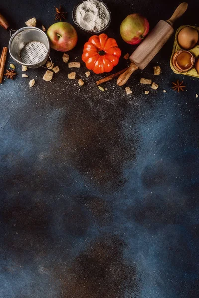 Sweet autumn baking cooking background with flour, rolling pin, decorative pumpkins, apples, cinnamon spices with anise cardamom sugar. Dark blue rusty background top view copy space