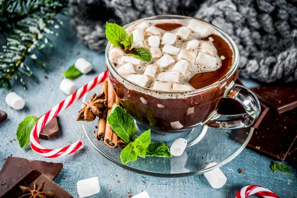 Homemade hot chocolate with mint, candy cane and marshmallow, light blue background with warm blanket, copy space