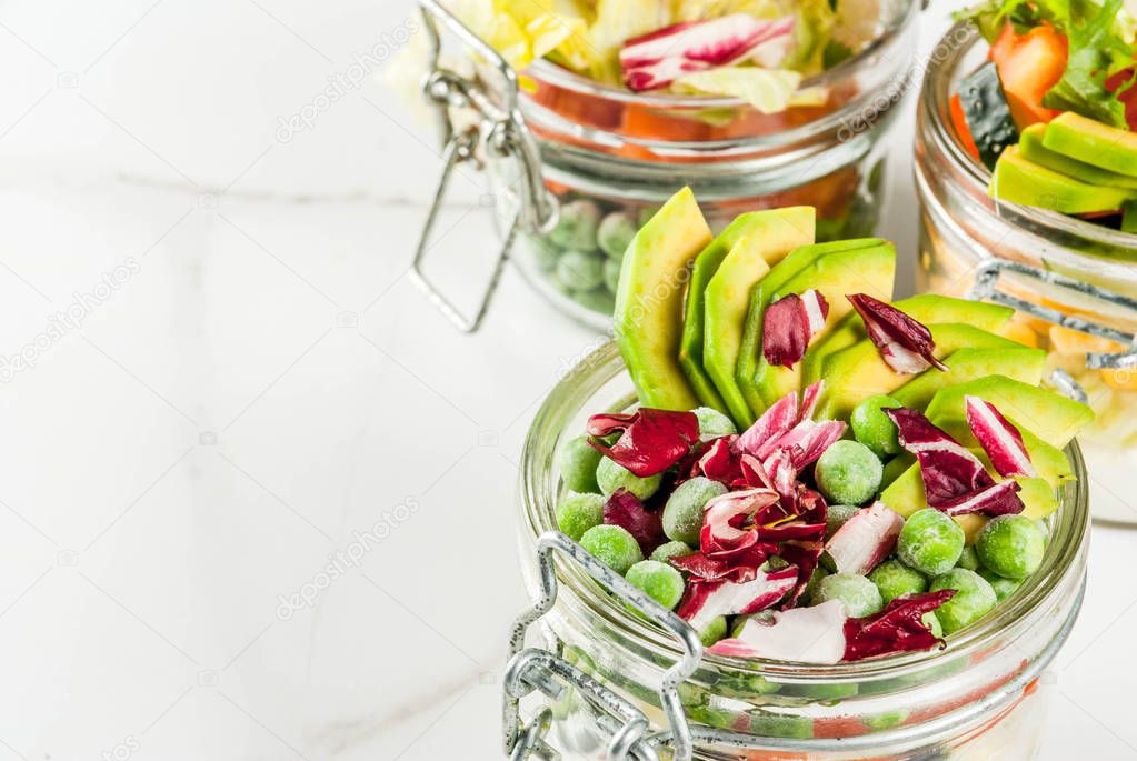 Fresh salads in jar with fresh vegetables and healthy dressings,  on white marble table, copy space