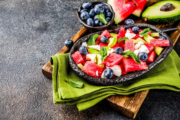 Summer food concept, fresh cold watermelon salad with feta cheese, blueberry, avocado and mint, dark rusty background copy space