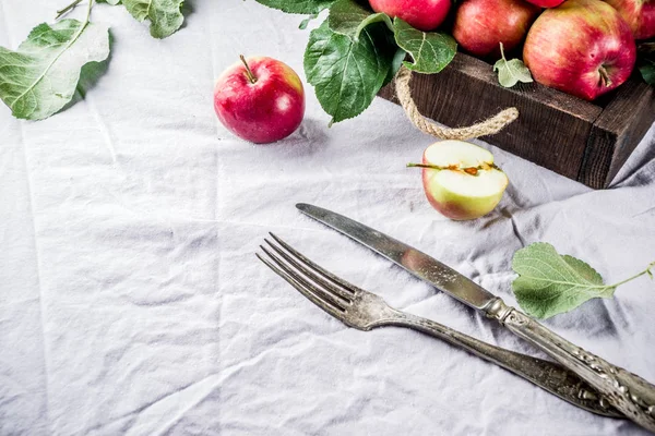Autumn food background with with a fork, a knife, fresh red apples with leaves, on a linen tablecloth table, copy space