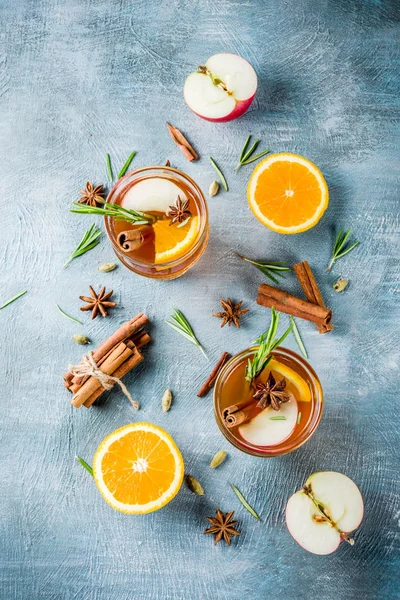 Traditional winter drinks, mulled wine cocktail with white wine, with spices, apple, orange. On a light blue table,