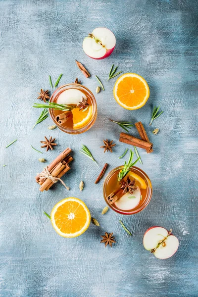 Traditional winter drinks, mulled wine cocktail with white wine, with spices, apple, orange. On a light blue table,