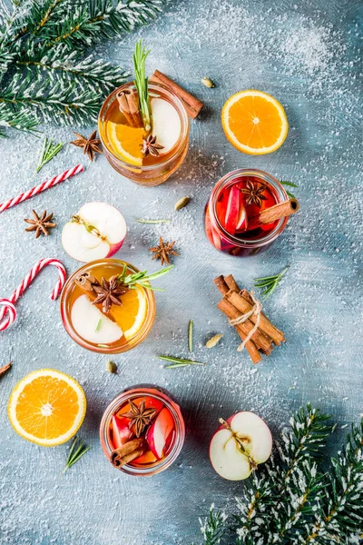 Traditional winter drinks, white and red mulled wine cocktail,  with white and red wine, spices, apple, orange. On a light blue table,
