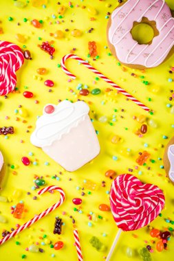 Tatlılar yaratıcı paralamak, lolipop, reçel, şeker, çerezleri çörek ve cupcakes, parlak sarı arka plana üstten görünüm kopya alanı ile tatlı kavramı