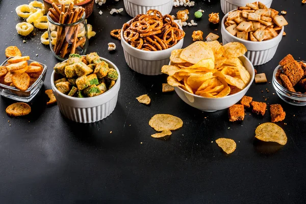 Variation different unhealthy snacks crackers, sweet salted popcorn, tortillas, nuts, straws, bretsels, back chalkboard copy space