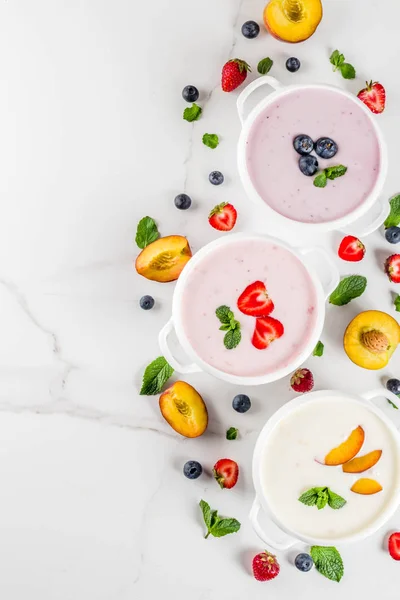 Summer healthy diet dinner, vegan food, dessert, various sweet creamy fruit & berry soups - strawberry, peach, blueberry, white marble background  copy space top view