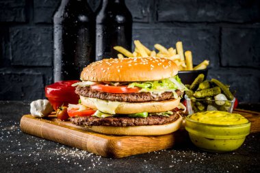 Çeşitli parti gıda, hamburger, patates kızartması, patates cipsi, salatalık turşusu, soğan, domates ve soğuk bira şişeleri, paslı siyah beton arka plan kopya alanı