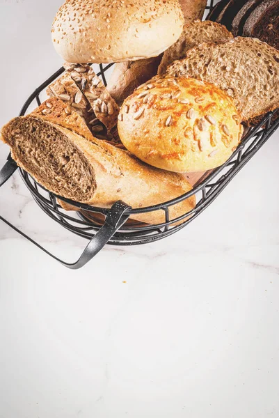 Variety of fresh homemade grain bread, in a metal basket, white marble background copy space