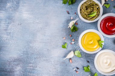 Otlar ve baharatlar ile dört klasik soslar - ketçap, mayonez, hardal, pesto - kümesi. Mavi beton zemin üstten görünüm kopya alanı