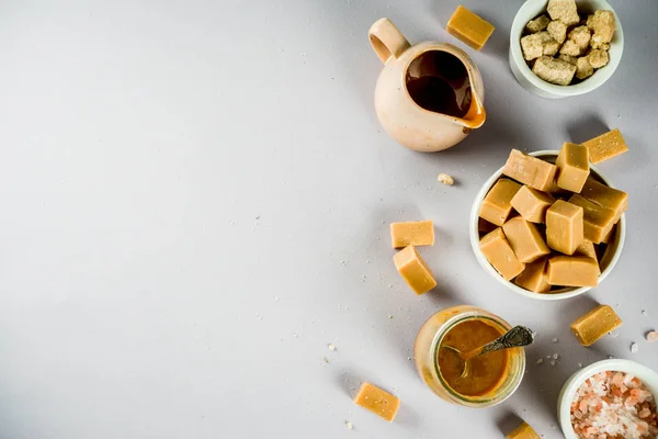 Salted caramel sauce with fudge candy, fleur de sel, brown cane sugar, grey background copy space top view