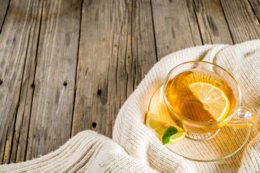 Sonbahar konfor ve sıcak kavramı. Çay cam bardağı limon, nane ve baharatlar, sıcak battaniye ile eski rustik ahşap arka plan üzerinde. Metin için yer kopyalayın