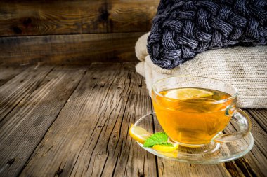 Sonbahar konfor ve sıcak kavramı. Çay cam bardağı limon, nane ve baharatlar, sıcak battaniye ile eski rustik ahşap arka plan üzerinde. Metin için yer kopyalayın
