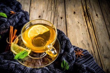 Sonbahar konfor ve sıcak kavramı. Çay cam bardağı limon, nane ve baharatlar, sıcak battaniye ile eski rustik ahşap arka plan üzerinde. Metin için yer kopyalayın