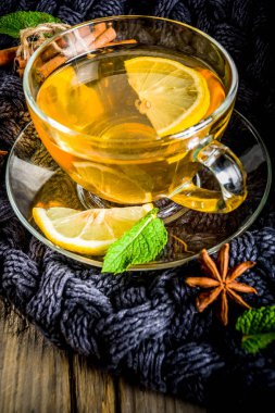 Sonbahar konfor ve sıcak kavramı. Çay cam bardağı limon, nane ve baharatlar, sıcak battaniye ile eski rustik ahşap arka plan üzerinde. Metin için yer kopyalayın