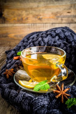 Sonbahar konfor ve sıcak kavramı. Çay cam bardağı limon, nane ve baharatlar, sıcak battaniye ile eski rustik ahşap arka plan üzerinde. Metin için yer kopyalayın