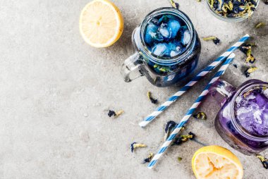 Sağlıklı yaz soğuk içecek, buzlu organik ve menekşe mavi kelebek bezelye çiçeği çayı limes ve limon, gri beton arka plan kopya alanı üstten görünüm