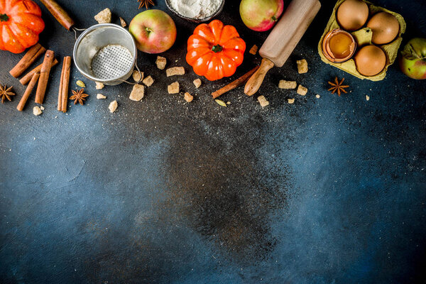 Sweet autumn baking concept, cooking background with baking accessories, flour, rolling pin, decorative pumpkins, apples, cinnamon spices with anise cardamom sugar. Dark blue rusty background top view copy space