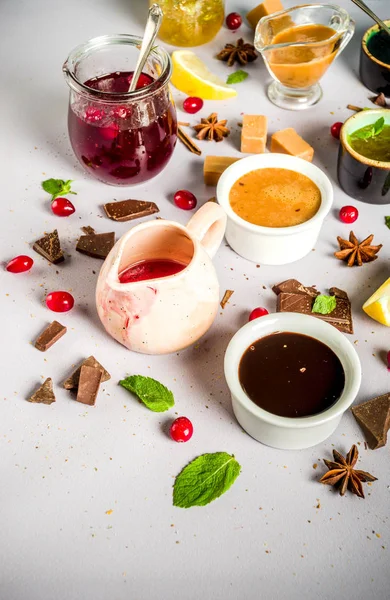 Various sweet sauces, toppings and syrups - lemon, orange, caramel, chocolate, cranberry, cherry, blueberry, on a light concrete background, top view copy space for text