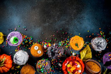 Cadılar Bayramı için komik çocuk davranır: varyasyonları cupcakes, farklı canavarlar, Cadılar, pumpkins, hayaletler şeklinde dekore edilmiştir. Karanlık paslı mavi arka plan kopya alanı için metin, üstten görünüm