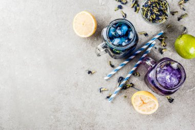 Sağlıklı yaz soğuk içecek, buzlu organik ve menekşe mavi kelebek bezelye çiçeği çayı limes ve limon, gri beton arka plan kopya alanı üstten görünüm
