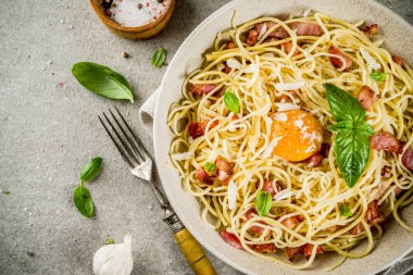 Geleneksel İtalyan Makarna, spagetti carbonara pastırma, krem sos, parmesan peyniri, yumurta sarısı ve taze fesleğen yaprakları gri taş arka plan kopya alanı