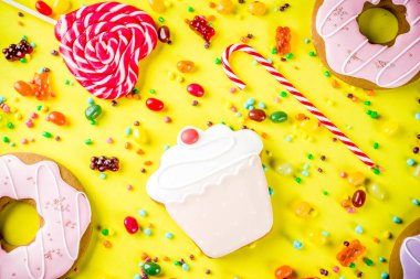 Tatlılar yaratıcı paralamak, lolipop, reçel, şeker, çerezleri çörek ve cupcakes, parlak sarı arka plana üstten görünüm kopya alanı ile tatlı kavramı
