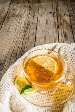 Sonbahar konfor ve sıcak kavramı. Çay cam bardağı limon, nane ve baharatlar, sıcak battaniye ile eski rustik ahşap arka plan üzerinde. Metin için yer kopyalayın