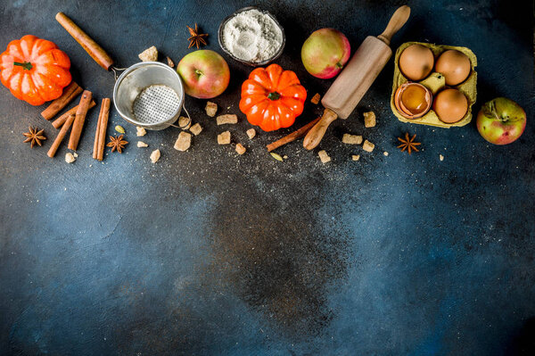 Sweet autumn baking concept, cooking background with baking accessories, flour, rolling pin, decorative pumpkins, apples, cinnamon spices with anise cardamom sugar. Dark blue rusty background top view copy space
