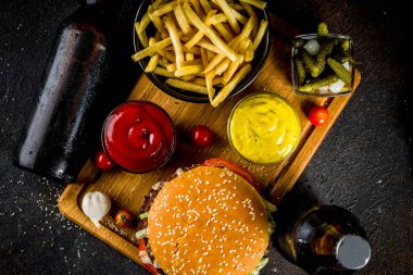 Çeşitli parti gıda, hamburger, patates kızartması, patates cipsi, salatalık turşusu, soğan, domates ve soğuk bira şişeleri, paslı siyah beton arka plan kopya alanı