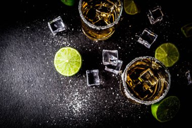 İki tekila shot bardağı buz küpleriyle koyu arka plan üzerine tuz ve limes alanı Kopyala