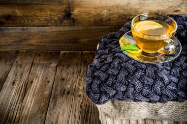 Sonbahar konfor ve sıcak kavramı. Çay cam bardağı limon, nane ve baharatlar, sıcak battaniye ile eski rustik ahşap arka plan üzerinde. Metin için yer kopyalayın