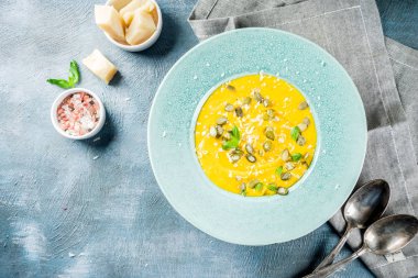 Balkabağı parmesan çorbası kabak çekirdeği, fesleğen yaprakları ve parmesan peyniri wit, mavi arka plan kopya alanı yukarıdan ışık