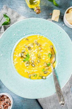 Balkabağı parmesan çorbası kabak çekirdeği, fesleğen yaprakları ve parmesan peyniri wit, mavi arka plan kopya alanı yukarıdan ışık