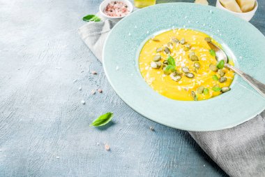 Balkabağı parmesan çorbası kabak çekirdeği, fesleğen yaprakları ve parmesan peyniri wit, mavi arka plan kopya alanı yukarıdan ışık