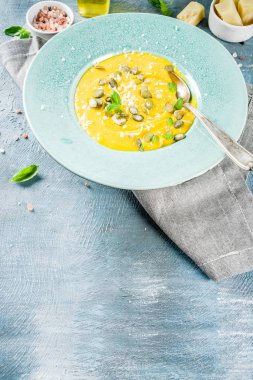 Balkabağı parmesan çorbası kabak çekirdeği, fesleğen yaprakları ve parmesan peyniri wit, mavi arka plan kopya alanı yukarıdan ışık