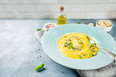 Balkabağı parmesan çorbası kabak çekirdeği, fesleğen yaprakları ve parmesan peyniri wit, mavi arka plan kopya alanı yukarıdan ışık