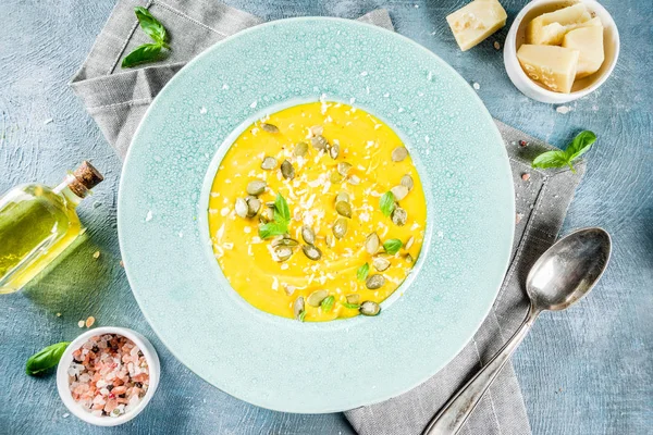 Balkabağı parmesan çorbası kabak çekirdeği, fesleğen yaprakları ve parmesan peyniri wit, mavi arka plan kopya alanı yukarıdan ışık