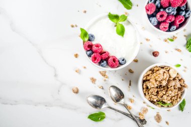 Sağlıklı snack veya kahvaltı fikir, ev yapımı organik Yunan yoğurt granola, ahududu, nane, yaban mersini beyaz mermer tablo görünümü top. 