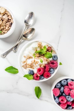 Sağlıklı snack veya kahvaltı fikir, ev yapımı organik Yunan yoğurt granola, ahududu, nane, yaban mersini beyaz mermer tablo görünümü top. 