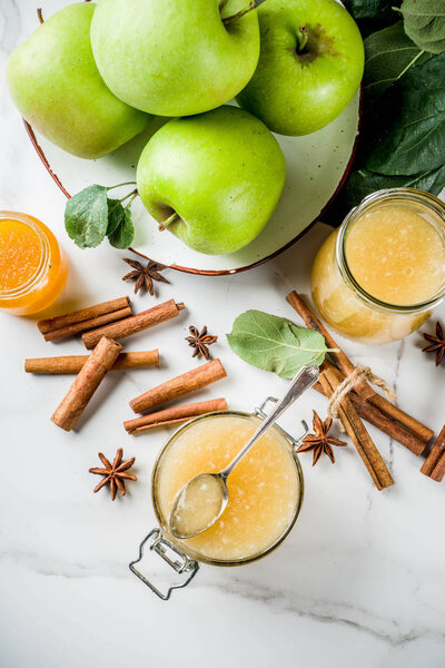 Homemade apple jam or sauce, with green apples and spices, white marble background copy space