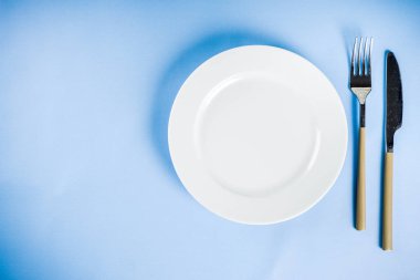 Bir tabak, çatal ve bıçak, üstten görünüm kopya alanı ile mavi arka plan