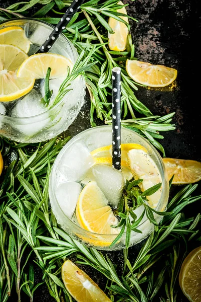 Cold lemonade or alcohol vodka cocktail with lemon and rosemary, On a black rusty metallic background, copy space top view