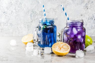 Sağlıklı yaz soğuk içecek, buzlu organik ve menekşe mavi kelebek bezelye çiçeği çayı limes ve limon, gri beton arka plan kopya alanı üstten görünüm