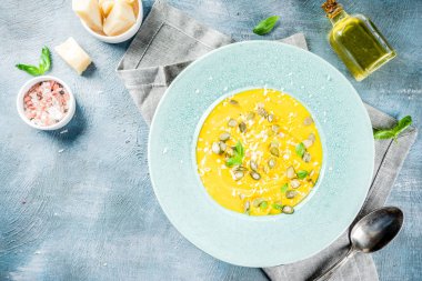 Balkabağı parmesan çorbası kabak çekirdeği, fesleğen yaprakları ve parmesan peyniri wit, mavi arka plan kopya alanı yukarıdan ışık