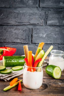Yaz sağlıklı snack meze, çeşitli renkli taze sebze (kereviz, ravent, biber, salatalık ve havuç) yoğurt sos daldırma, ahşap ve karanlık beton arka plan kopya alanı ile sopa