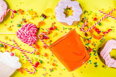 Cadılar Bayramı tatlılar kavramı, şenlikli bir kabak, şekerleme ve şeker, tanımlama bilgileri, reçel, tatlılar, parlak sarı arka plana üstten görünüm kopya alanı tam formunda kova