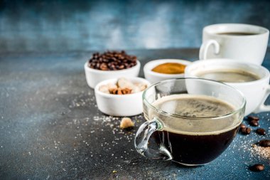 Üç kahve fincanı, fasulye, kahve ve kahverengi şeker zemin. Koyu mavi arka plan üstten görünüm alanı, metniniz için